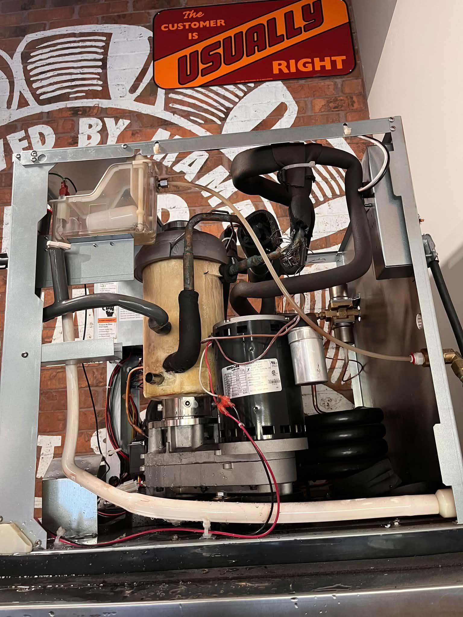 Open electrical appliance with wiring, metal components, and hoses inside a cabinet