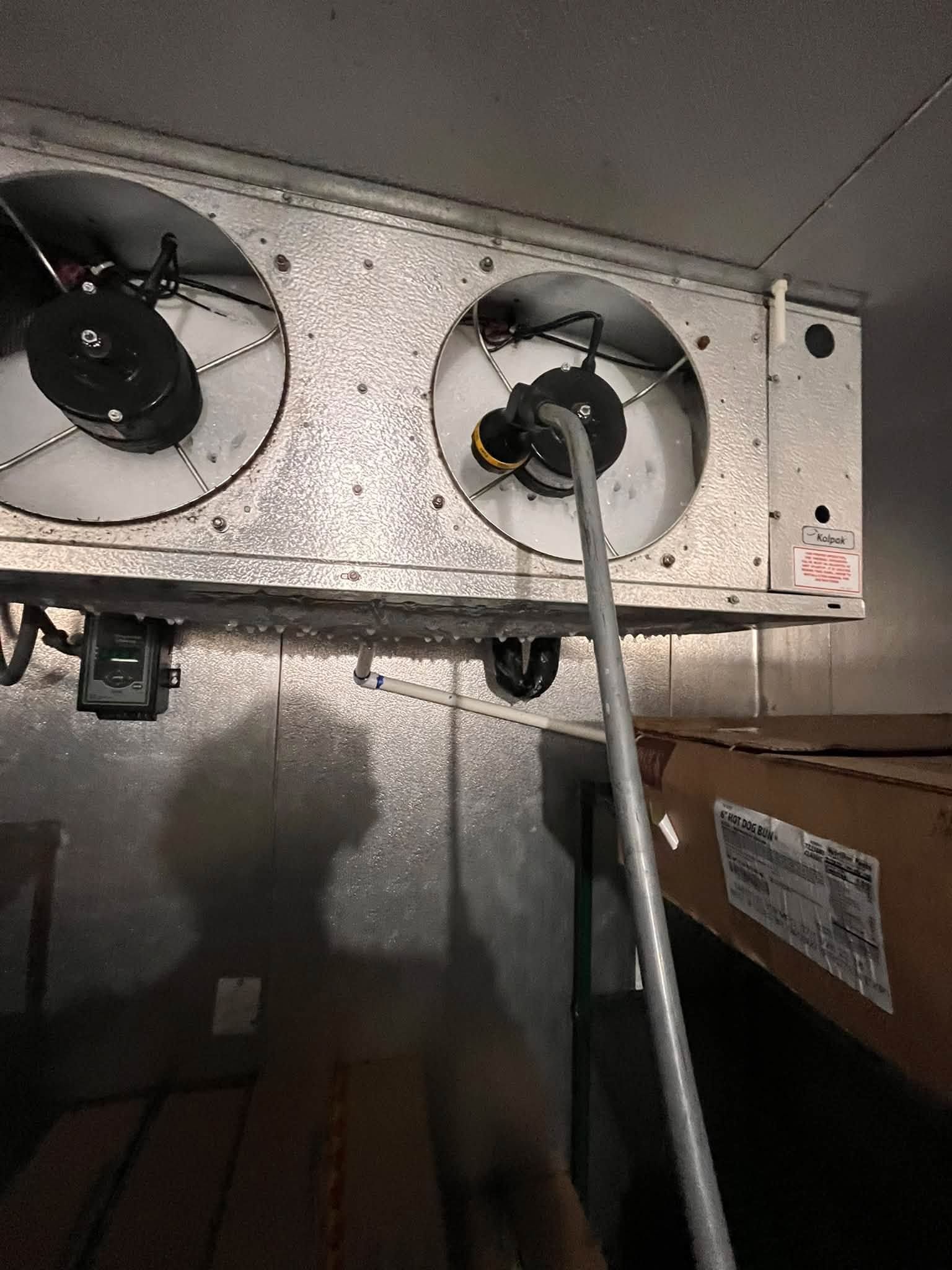 Metal HVAC vent with two fans and a cable hanging down in a dim mechanical space