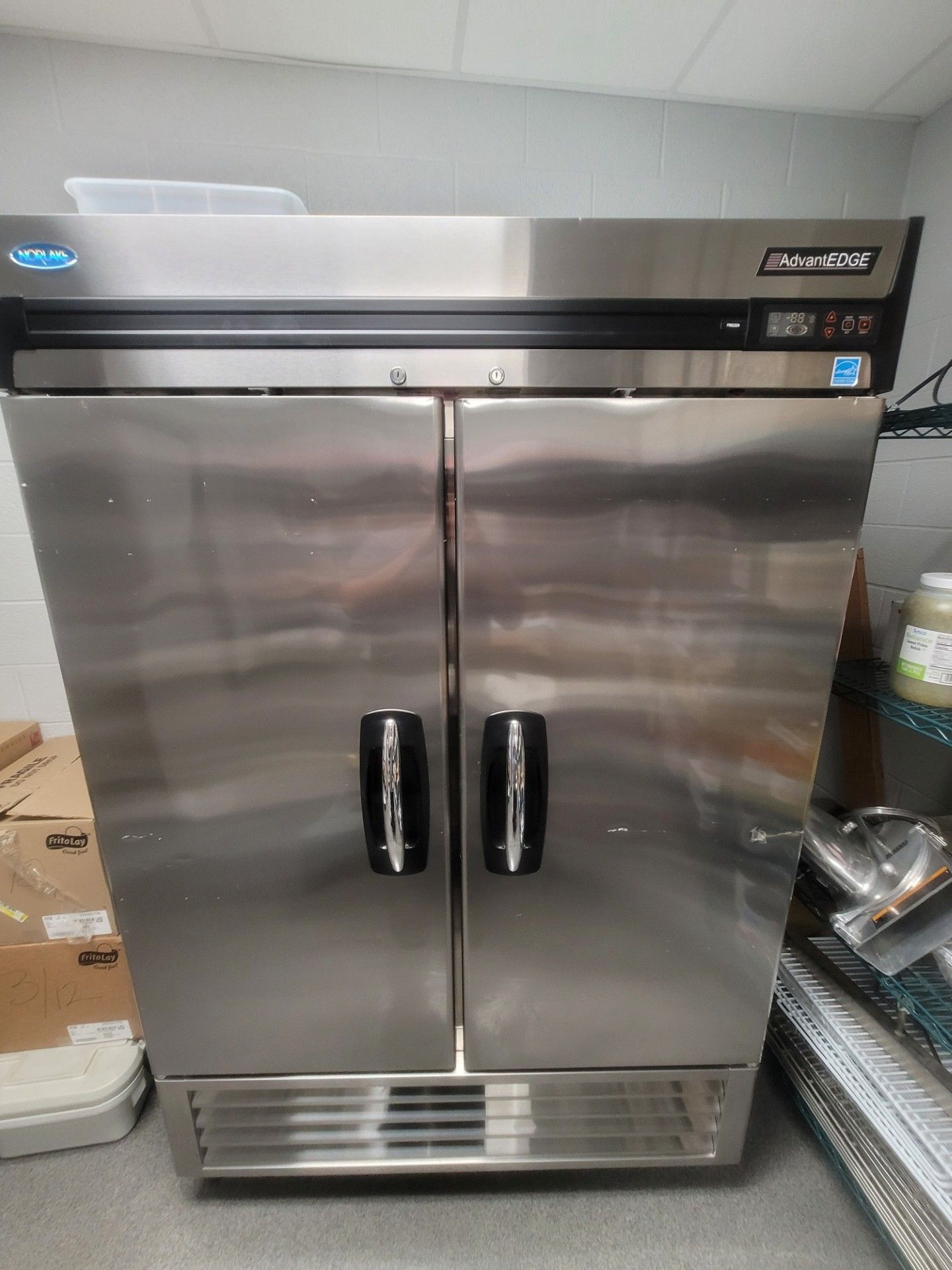 Stainless steel double-door commercial refrigerator in a kitchen or storage area.