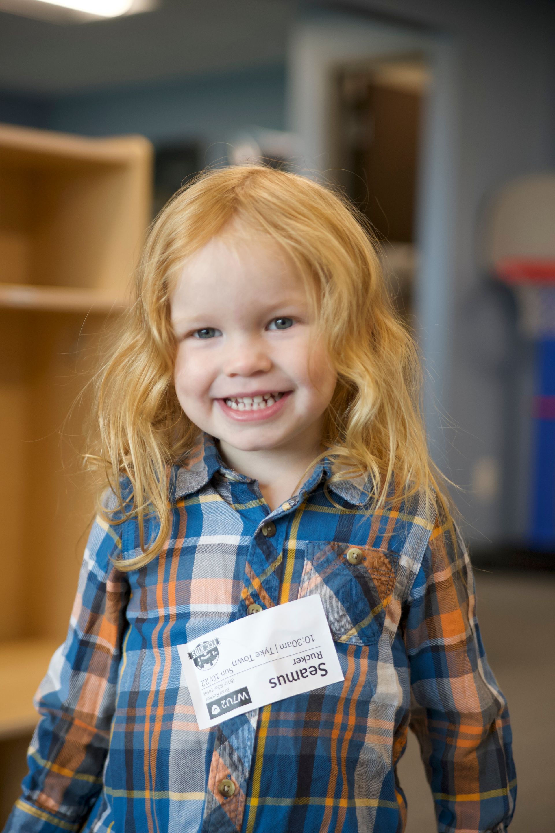 a little girl wearing a plaid shirt and a name tag is smiling for the camera .