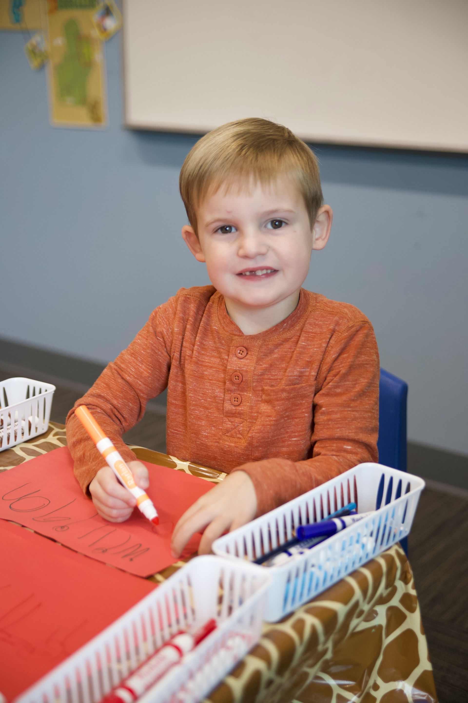 a young boy is sitting at a table with a marker in his hand .