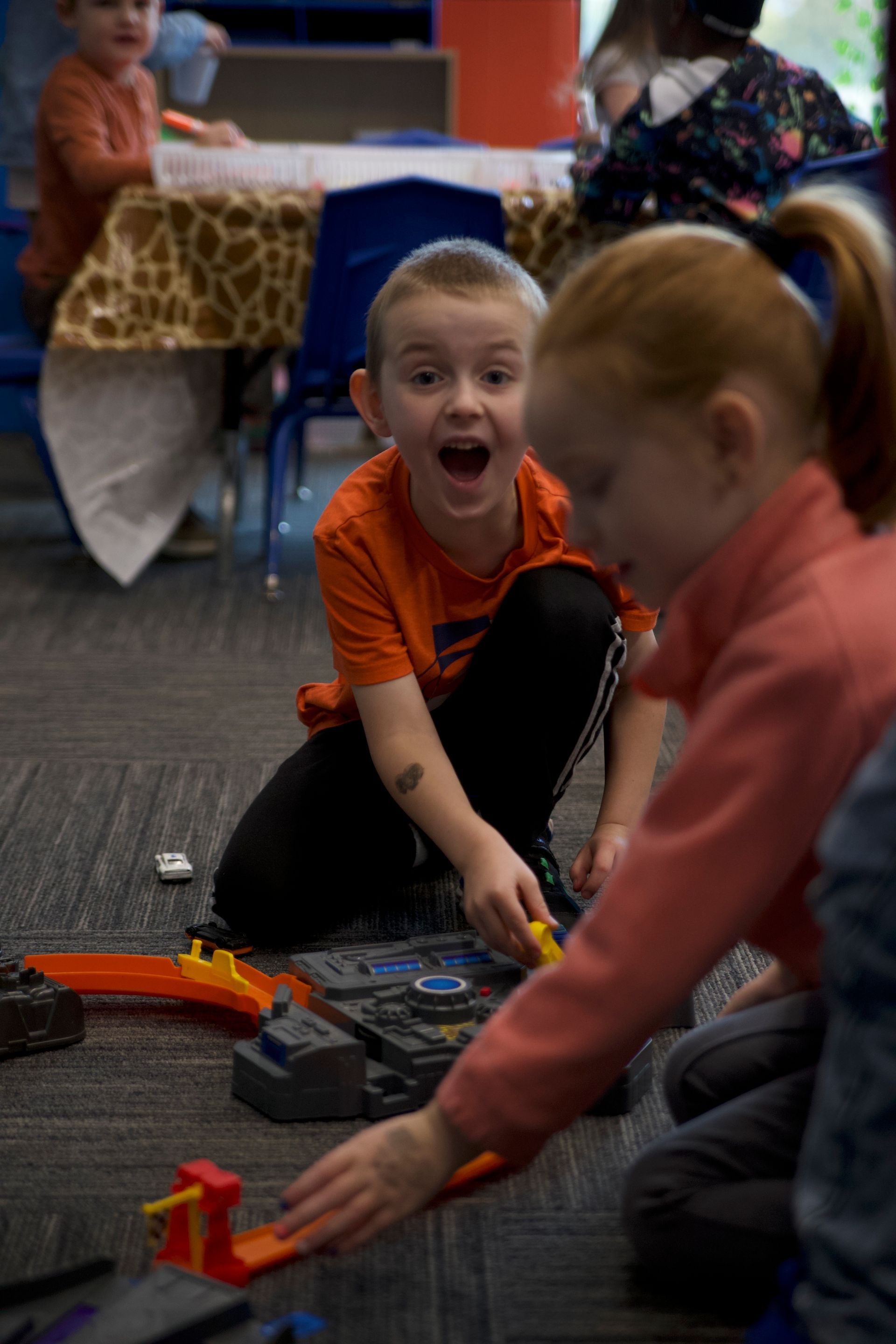 a boy and a girl are playing with a hot wheels track on the floor .
