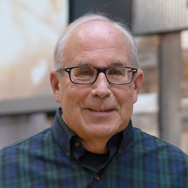 a man wearing glasses and a plaid shirt is smiling for the camera .