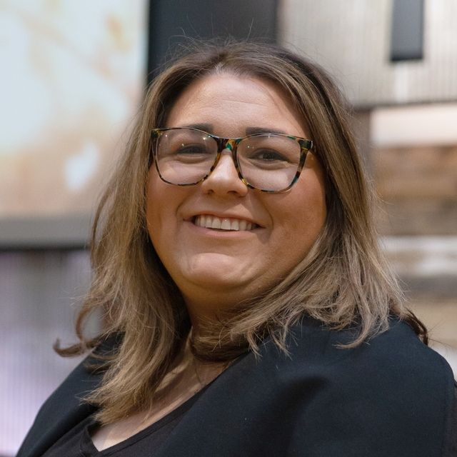 a woman wearing glasses and a black jacket is smiling for the camera .
