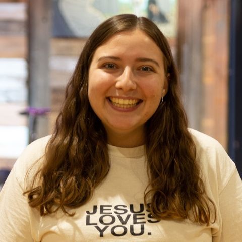 a woman wearing a jesus loves you t-shirt is smiling for the camera .