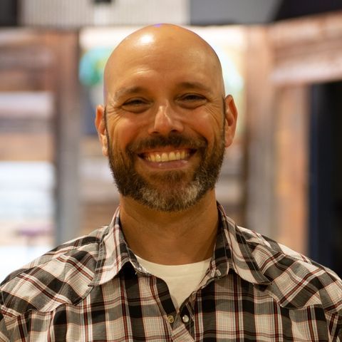 a bald man with a beard is wearing a plaid shirt and smiling .
