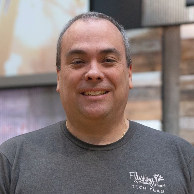 a man wearing a gray tech team shirt is smiling for the camera .