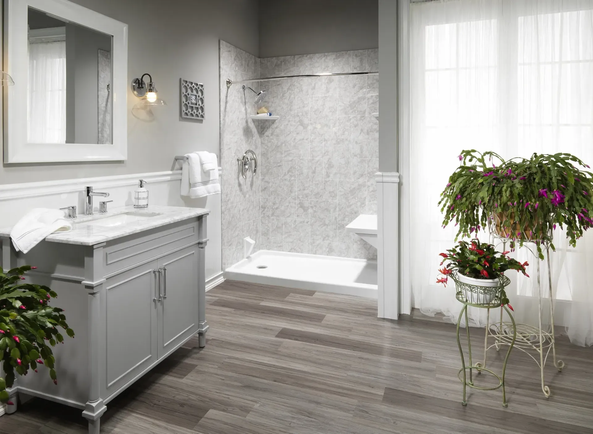 A gray themed bathroom with textured shower with seating, and some flowers on standing holders.