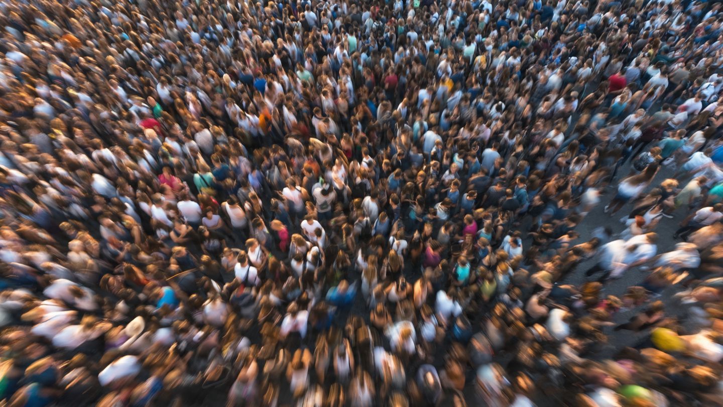 Dense crowd of people viewed from above, filling the frame in a blur of movement and color