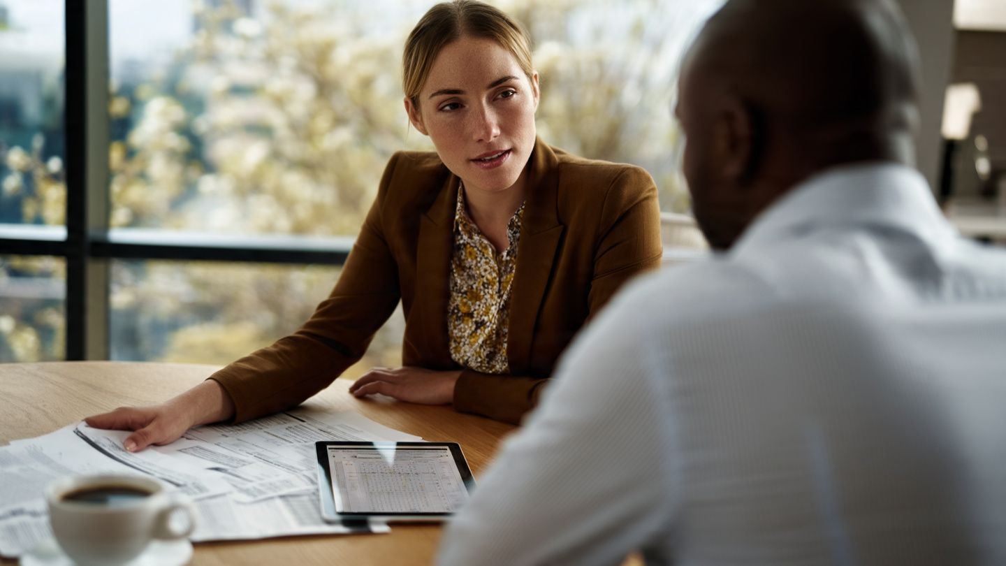 Two people in a meeting reviewing documents at a table by a bright window