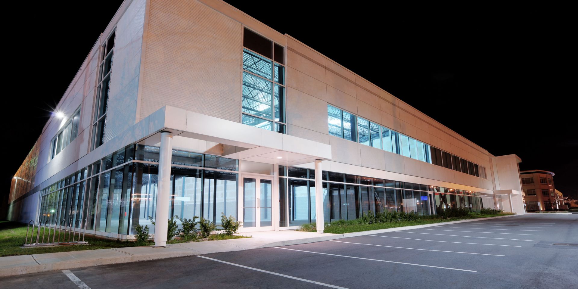 Modern commercial building at night with glass windows and a lit entryway.