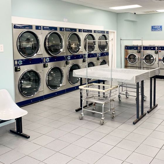 Click to learn more about Laundromats Laundromat with wall of washers & dryers, folding tables & rolling laundry baskets