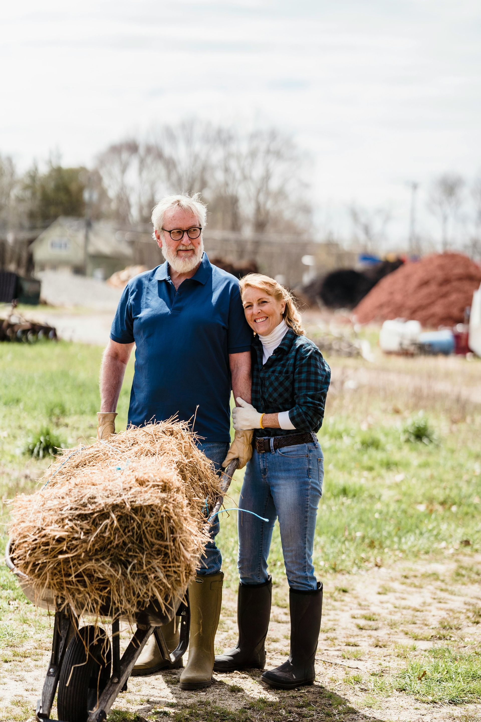 Couple beside a wheelbarrow of hay on a farm, smiling.