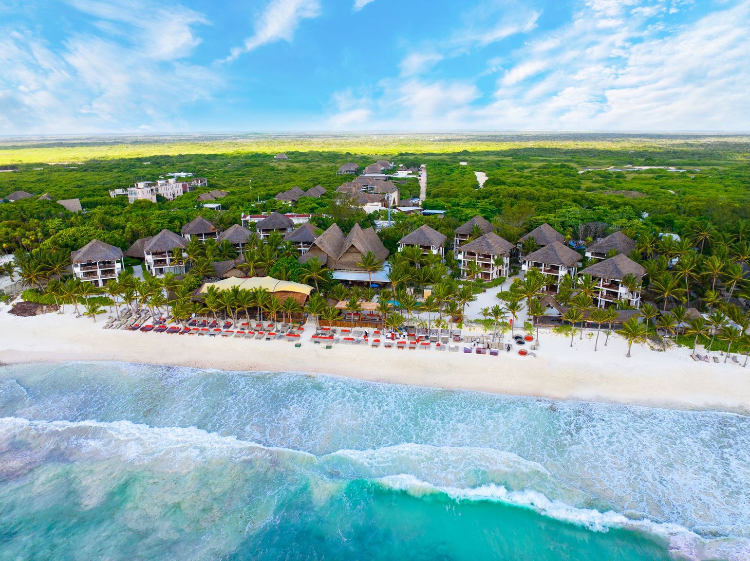 Aerial view of a tropical beachfront resort with white sand, turquoise waves, and palm trees