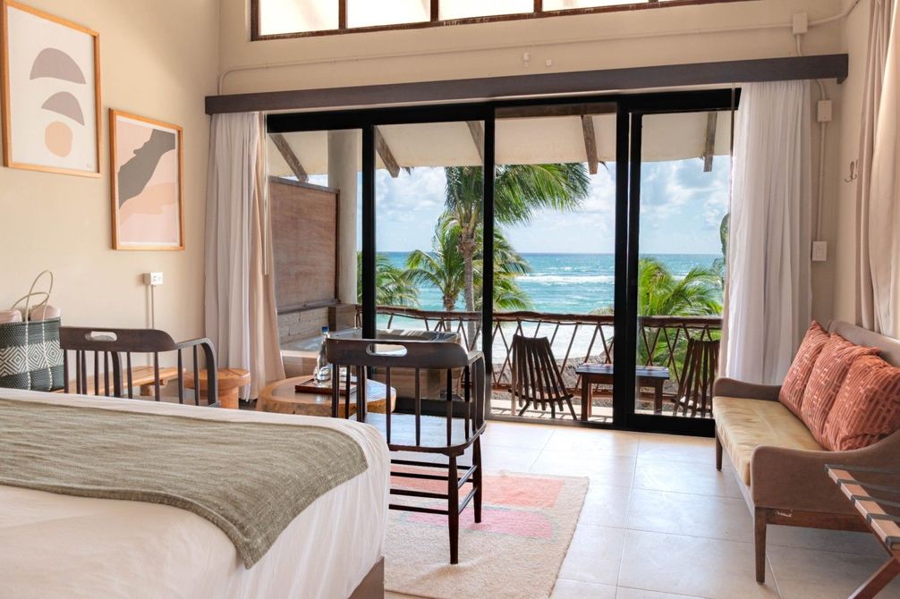 Bedroom with balcony doors overlooking the ocean, with a bed, desk, chair, and sofa inside