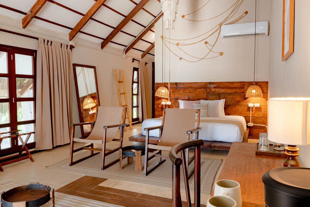 Cozy bedroom with a white bed, wooden ceiling beams, chairs, and warm bedside lamps