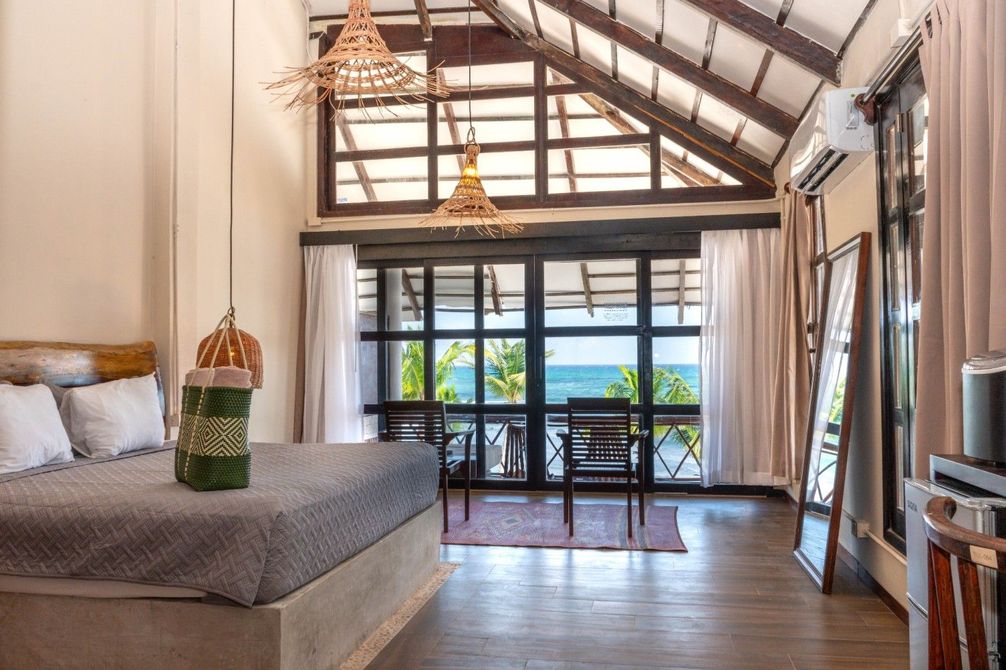 Bright bedroom with a king bed, high wood ceiling, and balcony view of the ocean