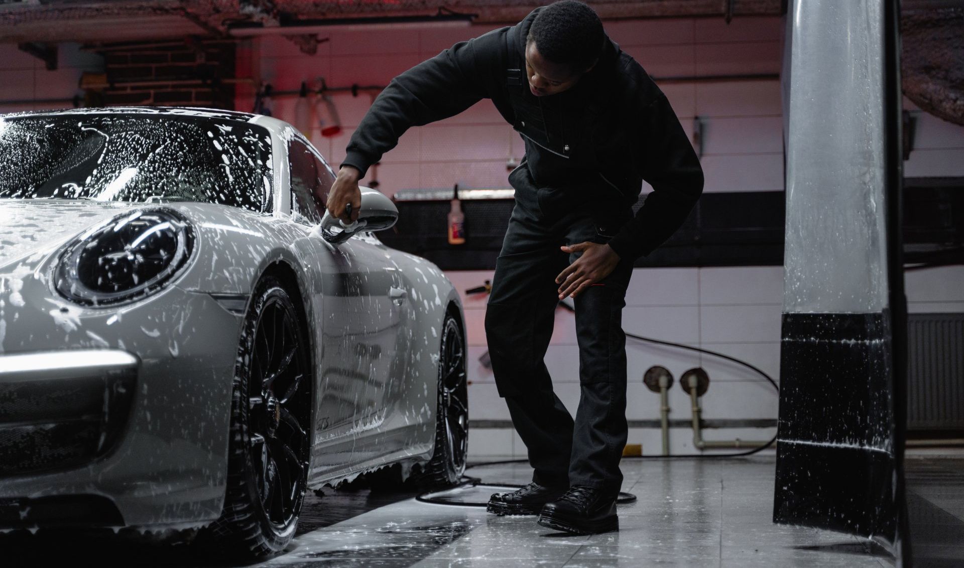 Detailing worker washing a silver sports car with soap in a garage