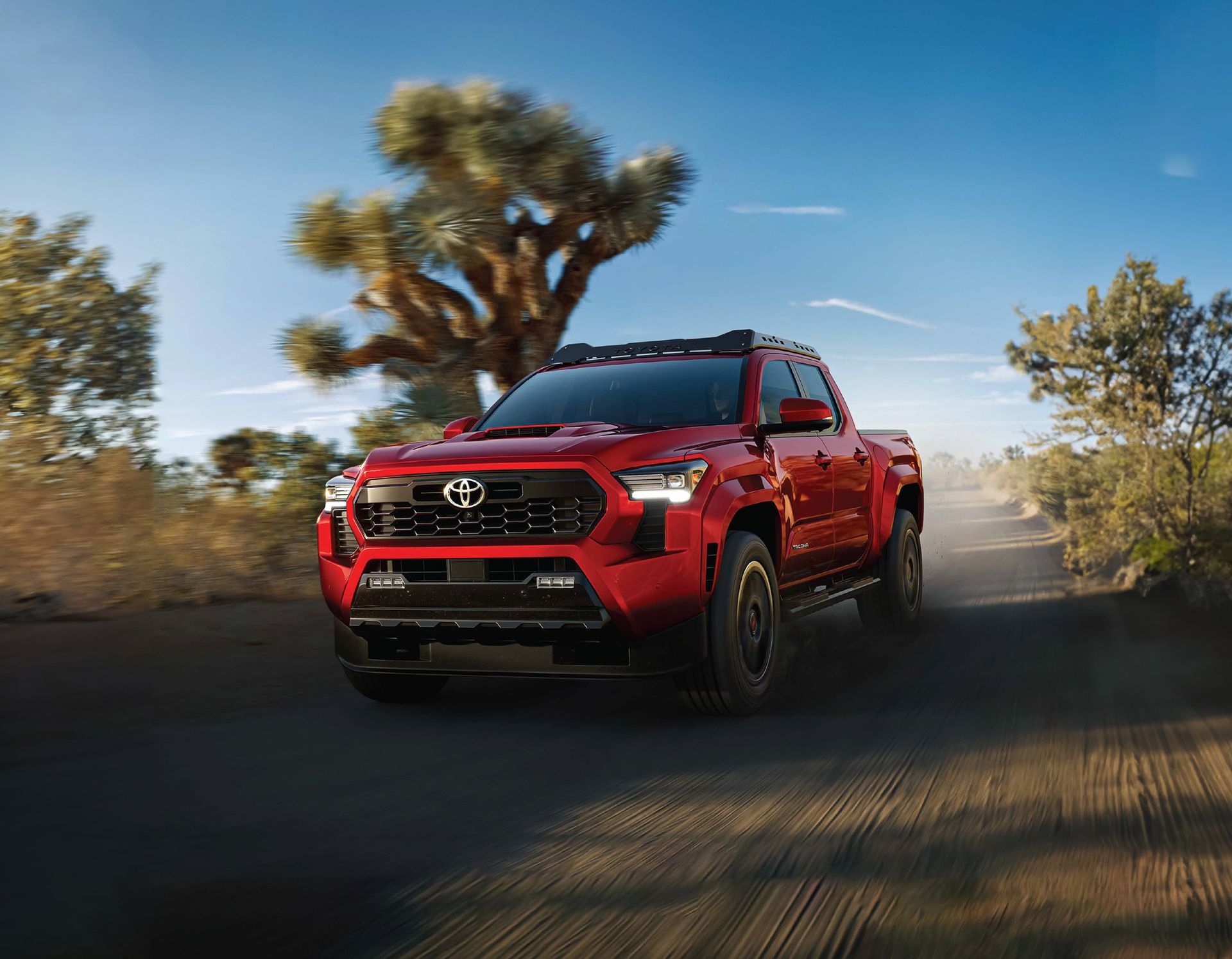 Camioneta Toyota roja a toda velocidad por una carretera desértica, levantando polvo bajo un cielo azul despejado.