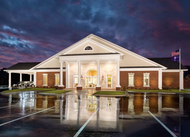Front view of a brick building with white columns at dusk, reflected on wet pavement
