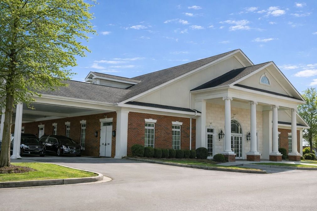 Large beige brick building with white columns and a covered drive-through entrance under a blue sky