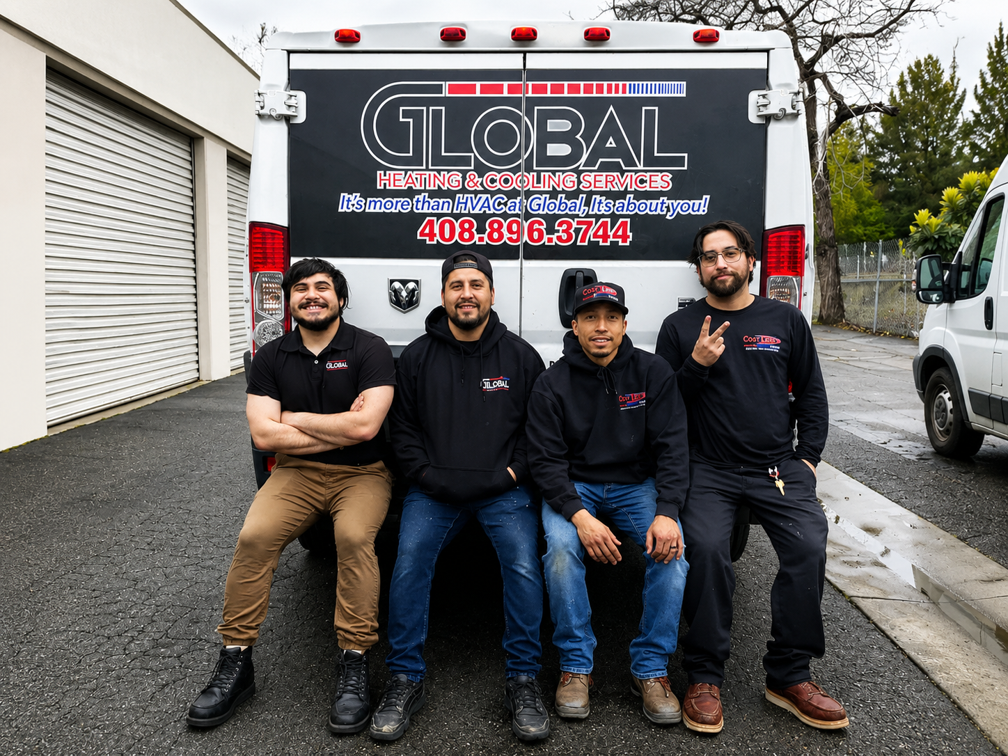 Five workers in black shirts sit in front of a Global Moving truck on a wet driveway.