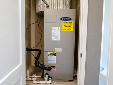 HVAC unit in a closet with exposed pipes, wiring, and a yellow service label.