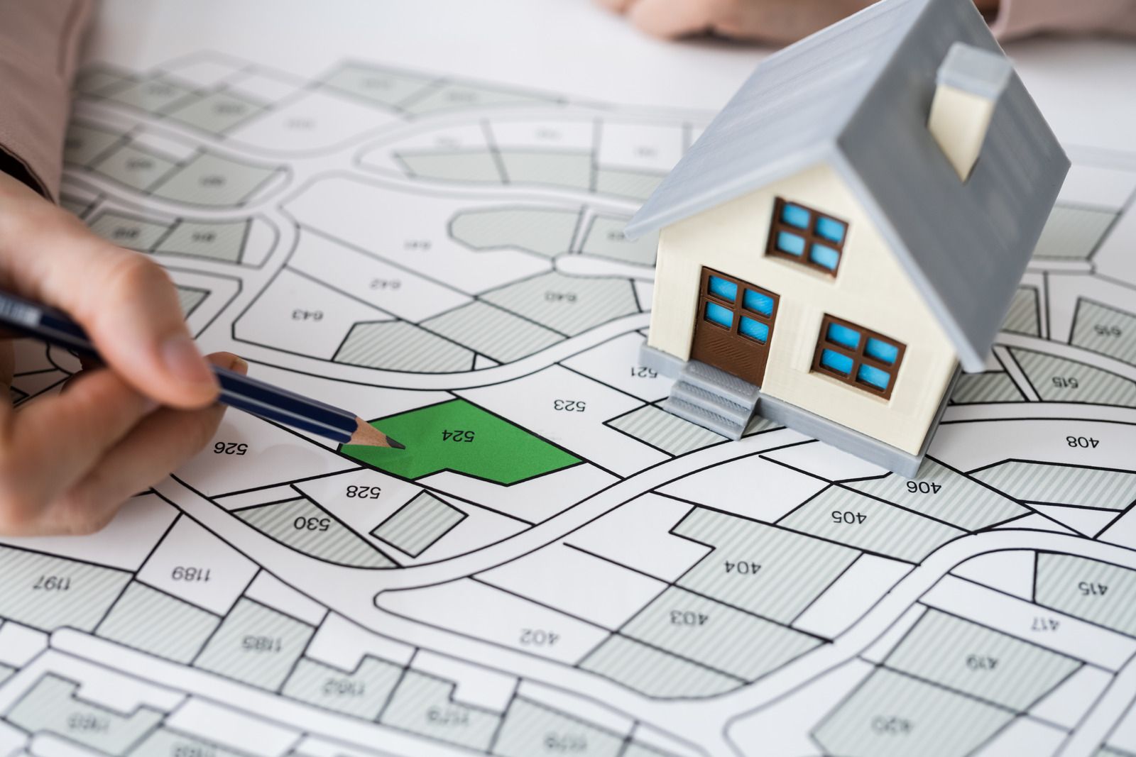 A person is drawing a house on a map with a pencil.
