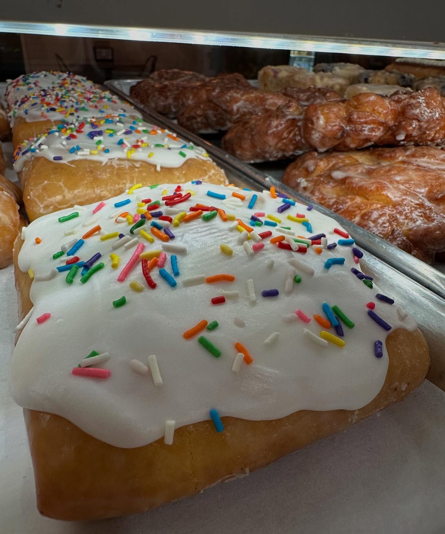 Donuts in a bakery case, frosted with sprinkles.