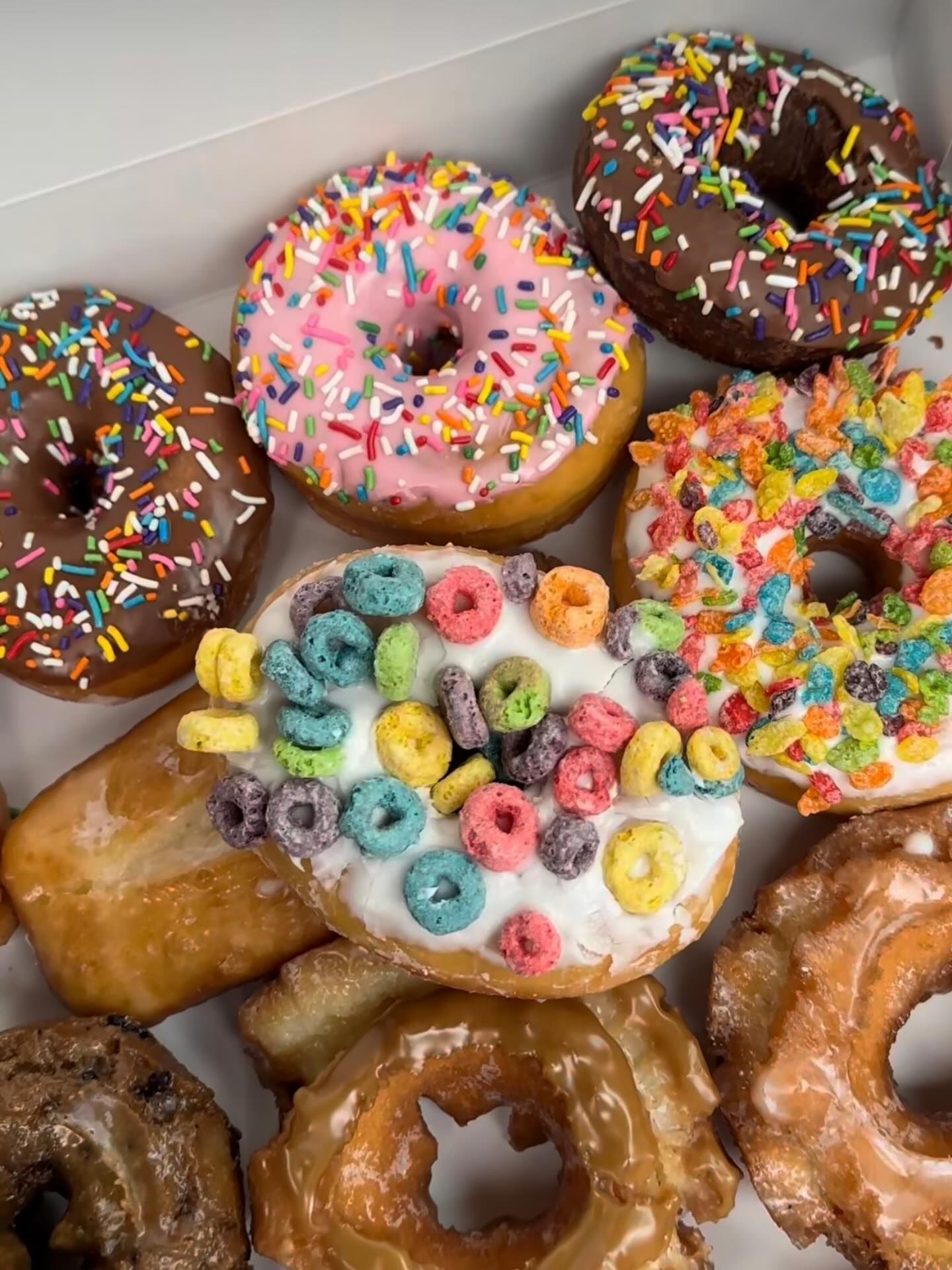 Box of assorted donuts with colorful frosting and sprinkles.