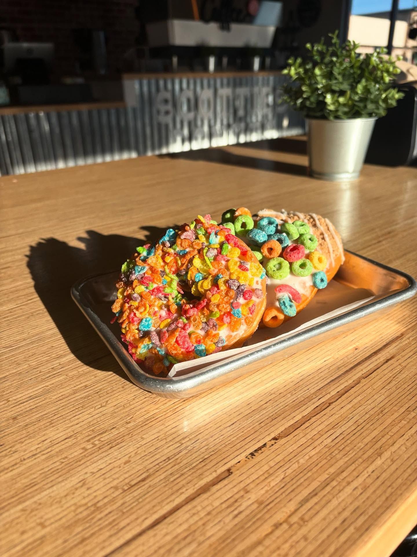 Two colorful donuts on a silver tray, placed on a wood table, in a cafe setting.