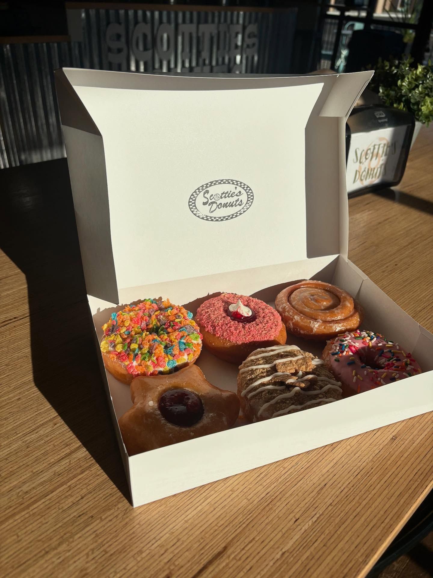 Box of colorful donuts on a wooden table. The box has a logo on the lid.