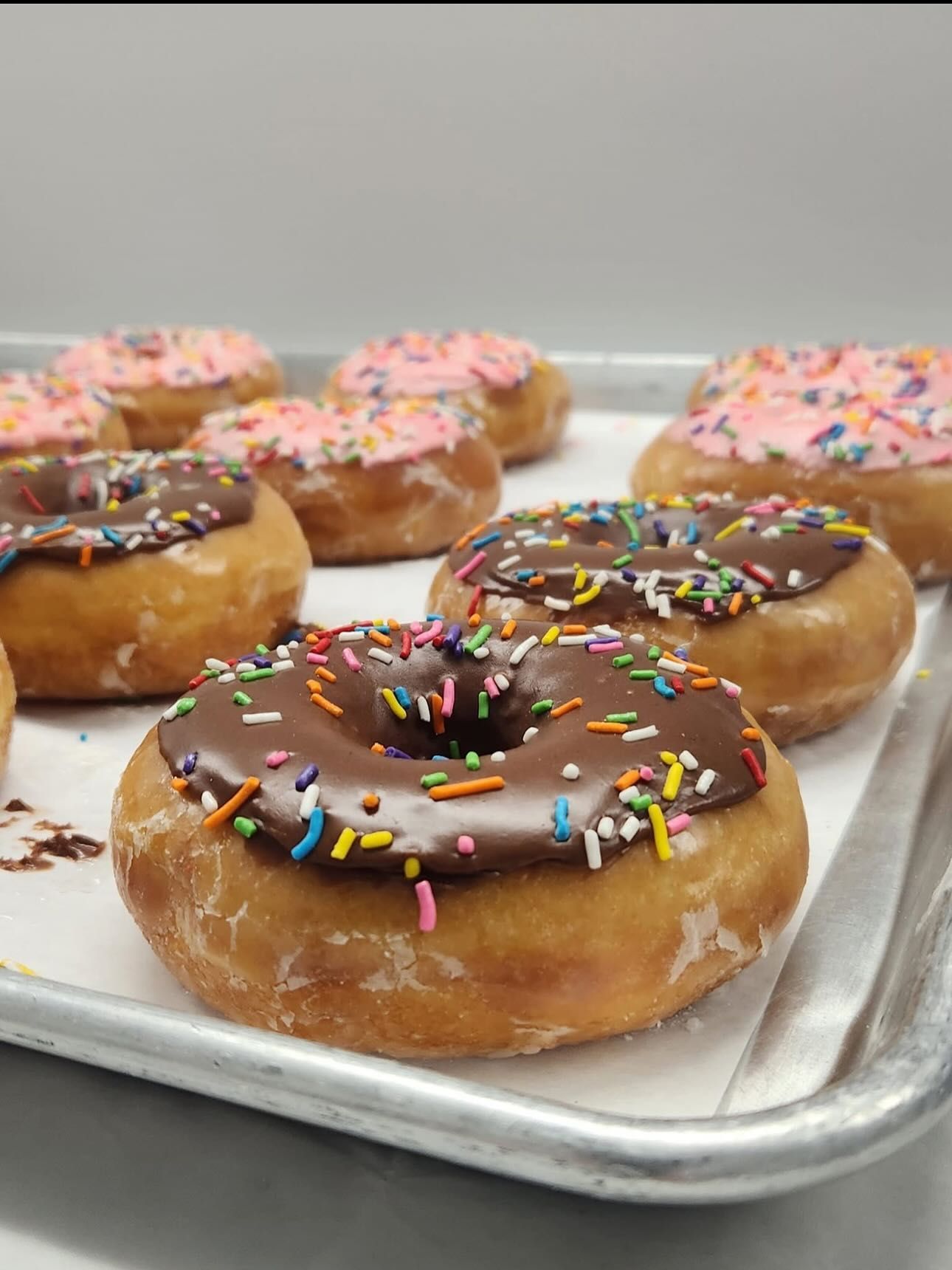 Donuts on a tray with chocolate and pink frosting, rainbow sprinkles.