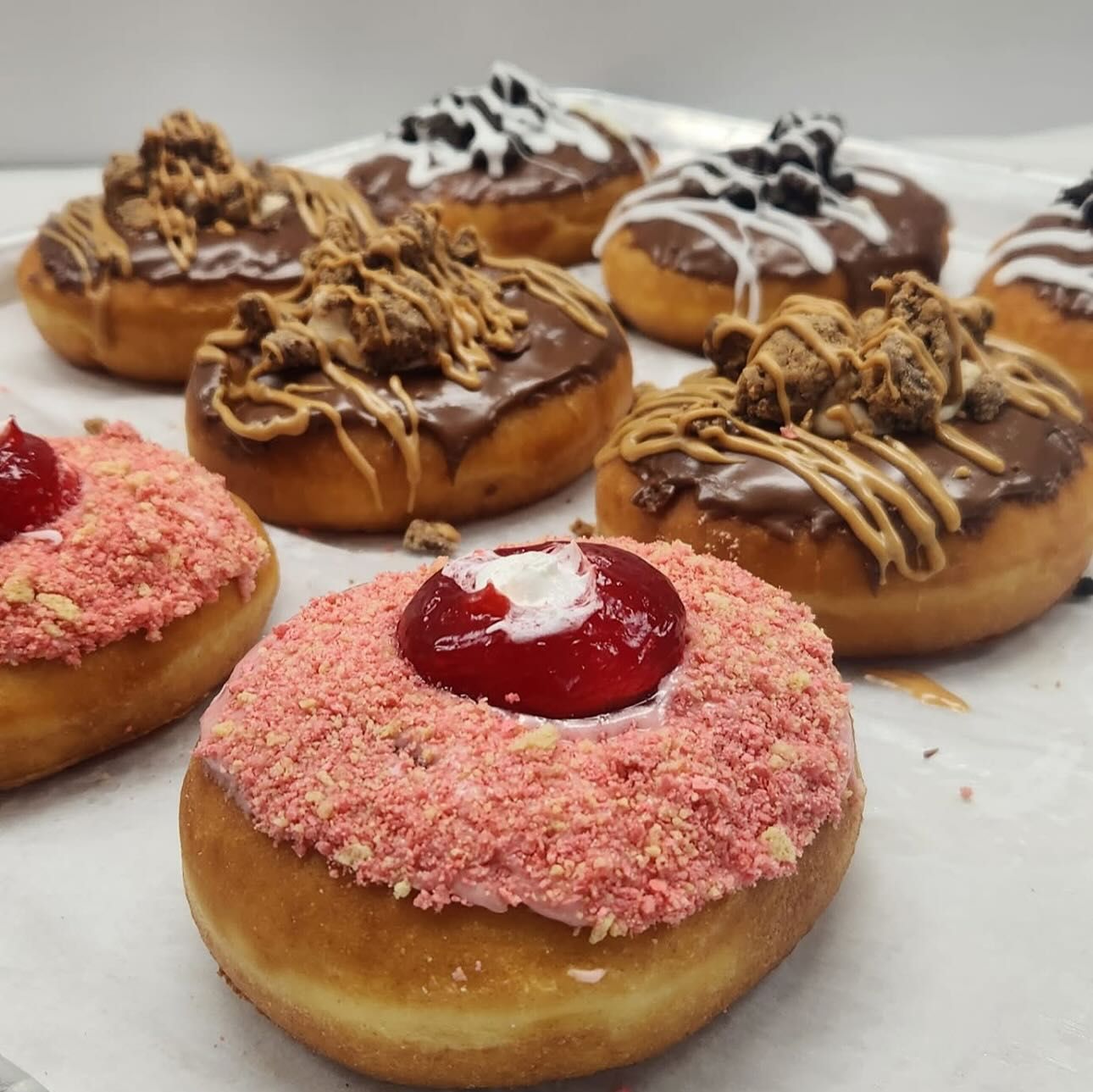 Assortment of glazed donuts with various toppings: cookies, candy, and pink strawberry crumble.