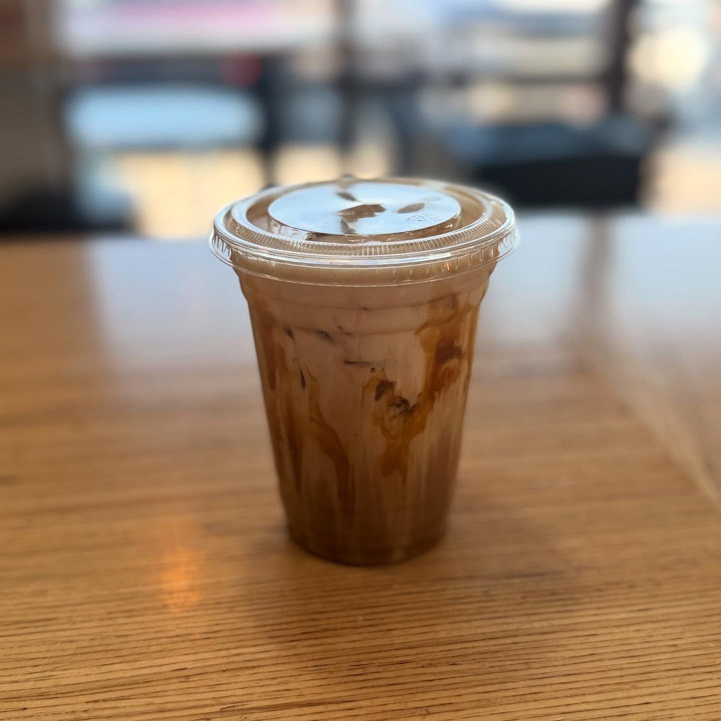 Iced coffee in a clear plastic cup with caramel drizzle and a smiley face on the lid.