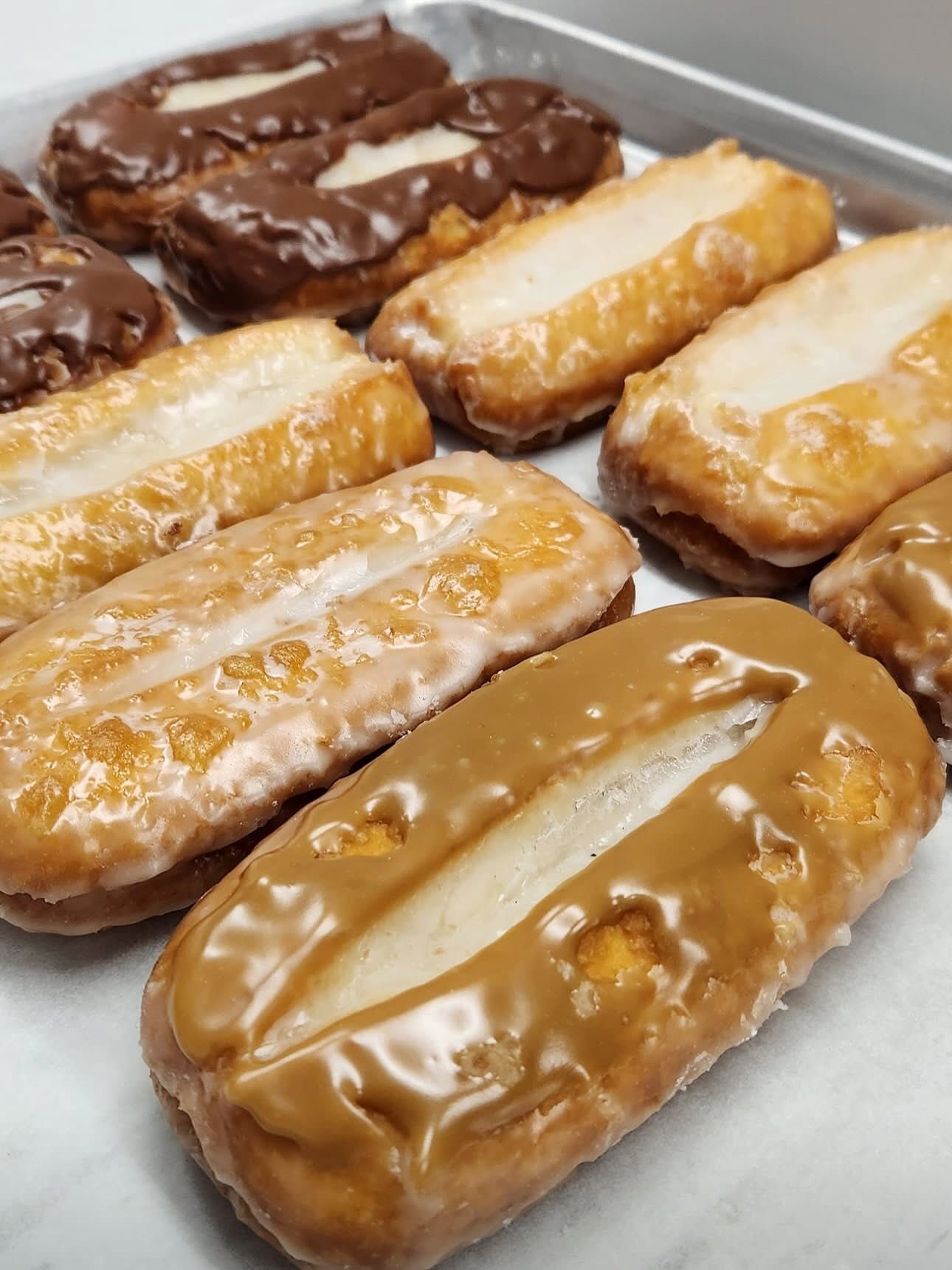 Tray of rectangular glazed donuts, some with chocolate or caramel frosting.