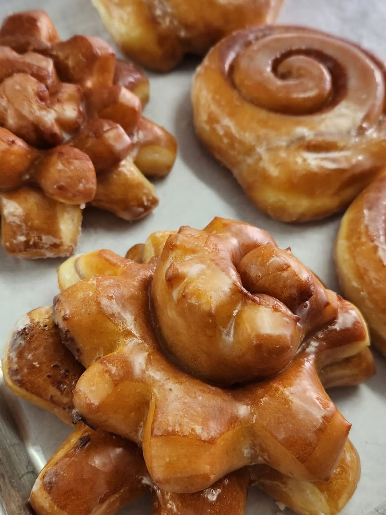 Assortment of glazed donuts: spiral, cluster, and ring shapes, light brown with shiny glaze.