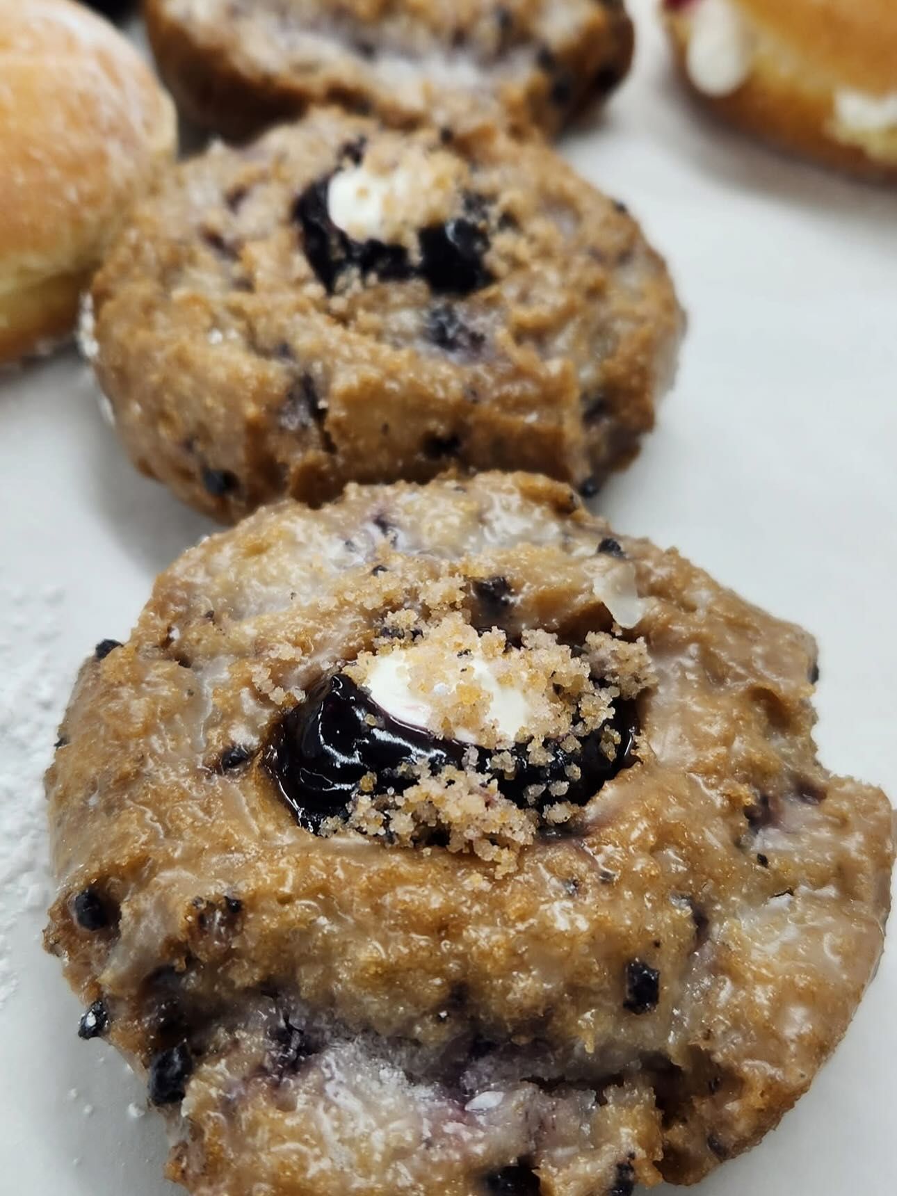 Close-up of glazed blueberry donuts with crumble topping on a white plate.