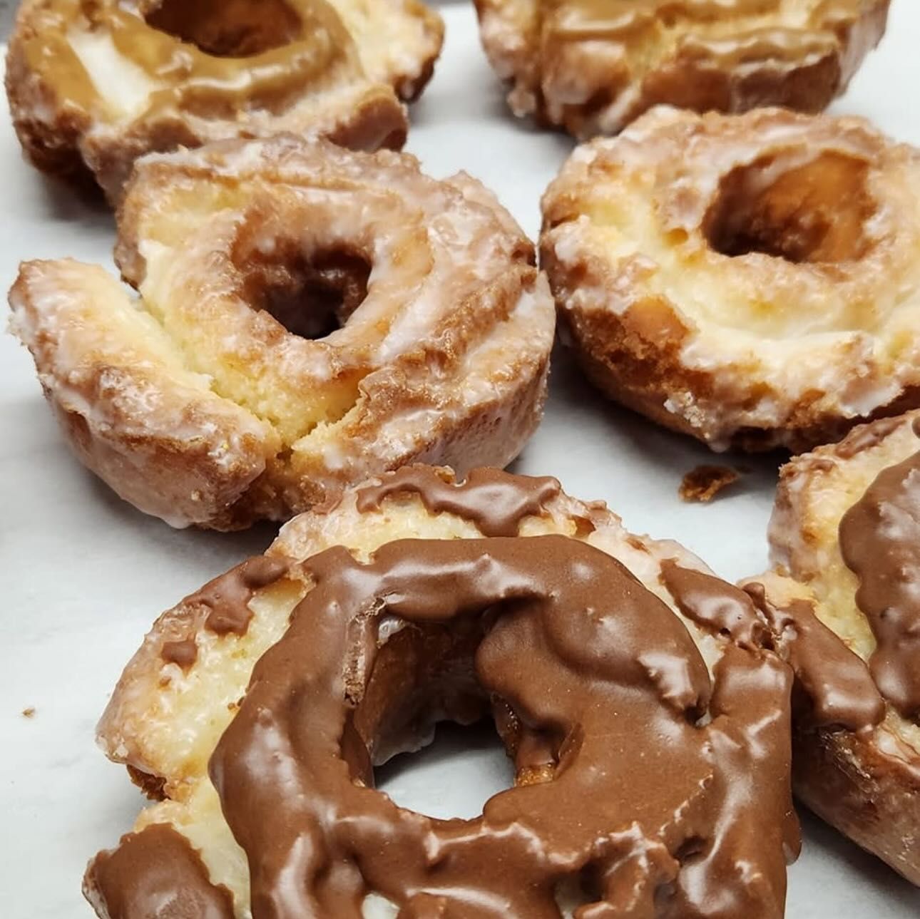 Glazed donuts, some with chocolate frosting, arranged on a surface.