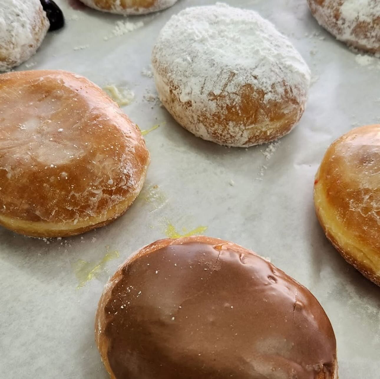 Close-up of glazed, powdered sugar, and chocolate frosted donuts on parchment paper.