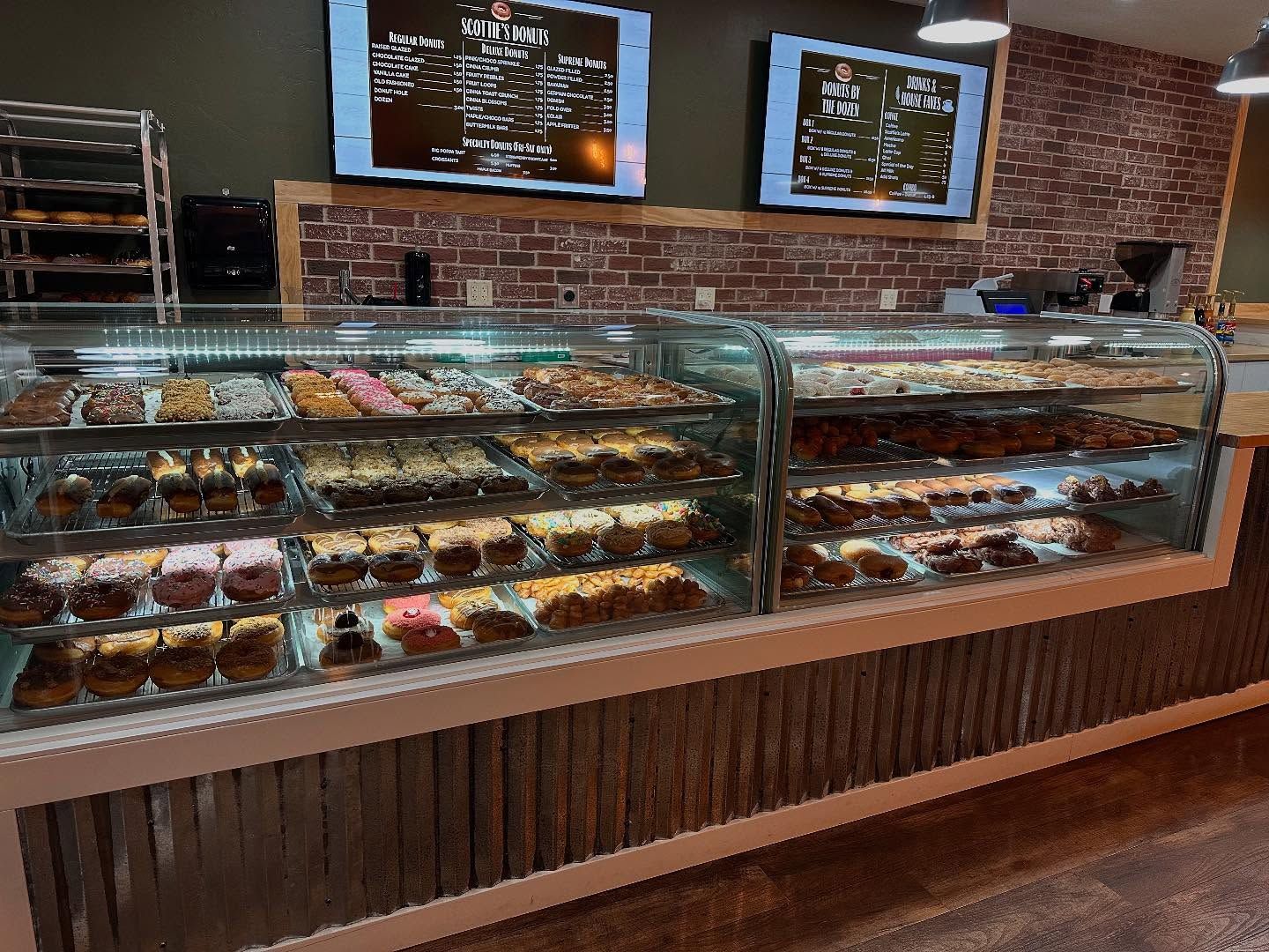 Bakery display case filled with pastries, brick wall backdrop, menus on screens.