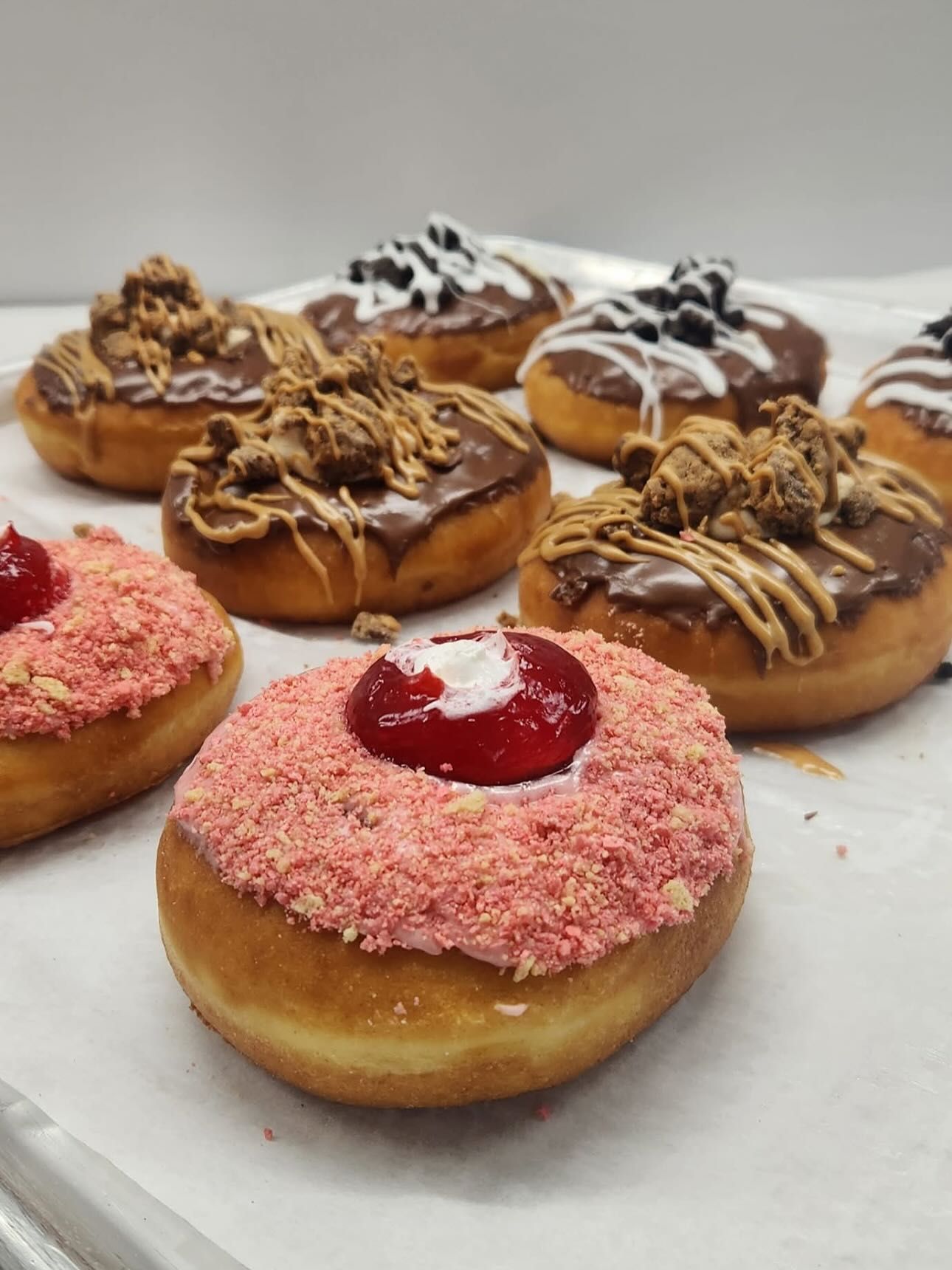 Donuts with various toppings, including chocolate frosting, sprinkles, and fruit, on a white surface.