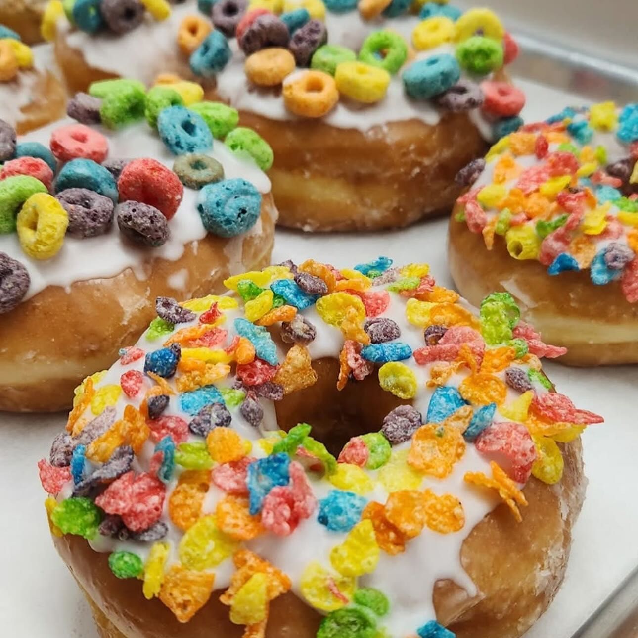 Donuts with white glaze, topped with colorful cereal pieces. Close-up on several baked goods.