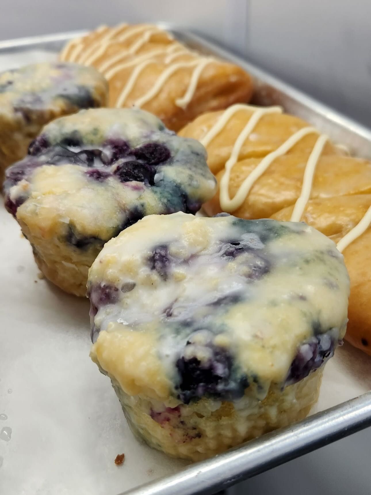 Blueberry muffins and pastries with glaze on a metal tray.