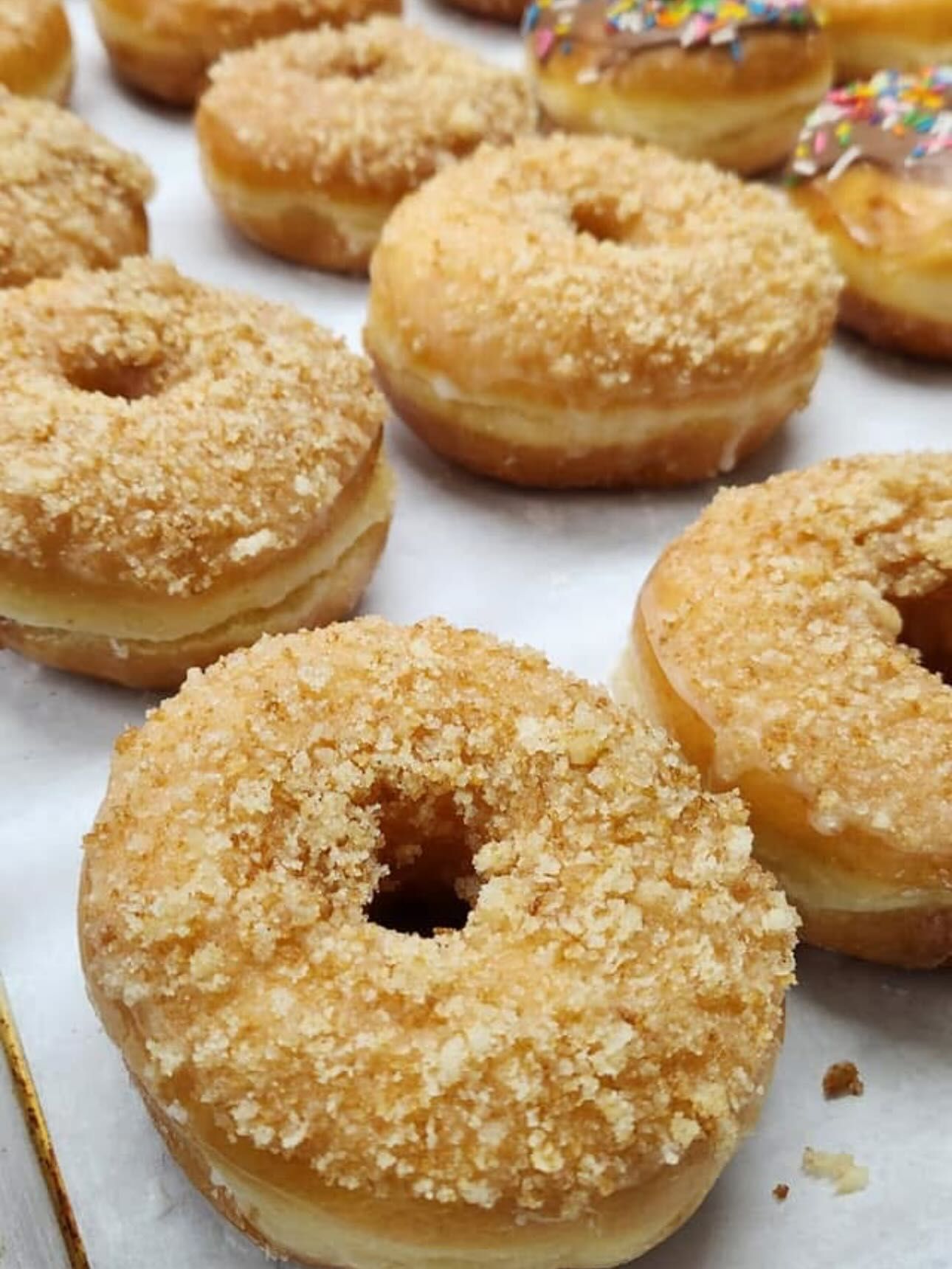 Close-up of glazed donuts with various toppings, including crumbles and sprinkles, on white surface.