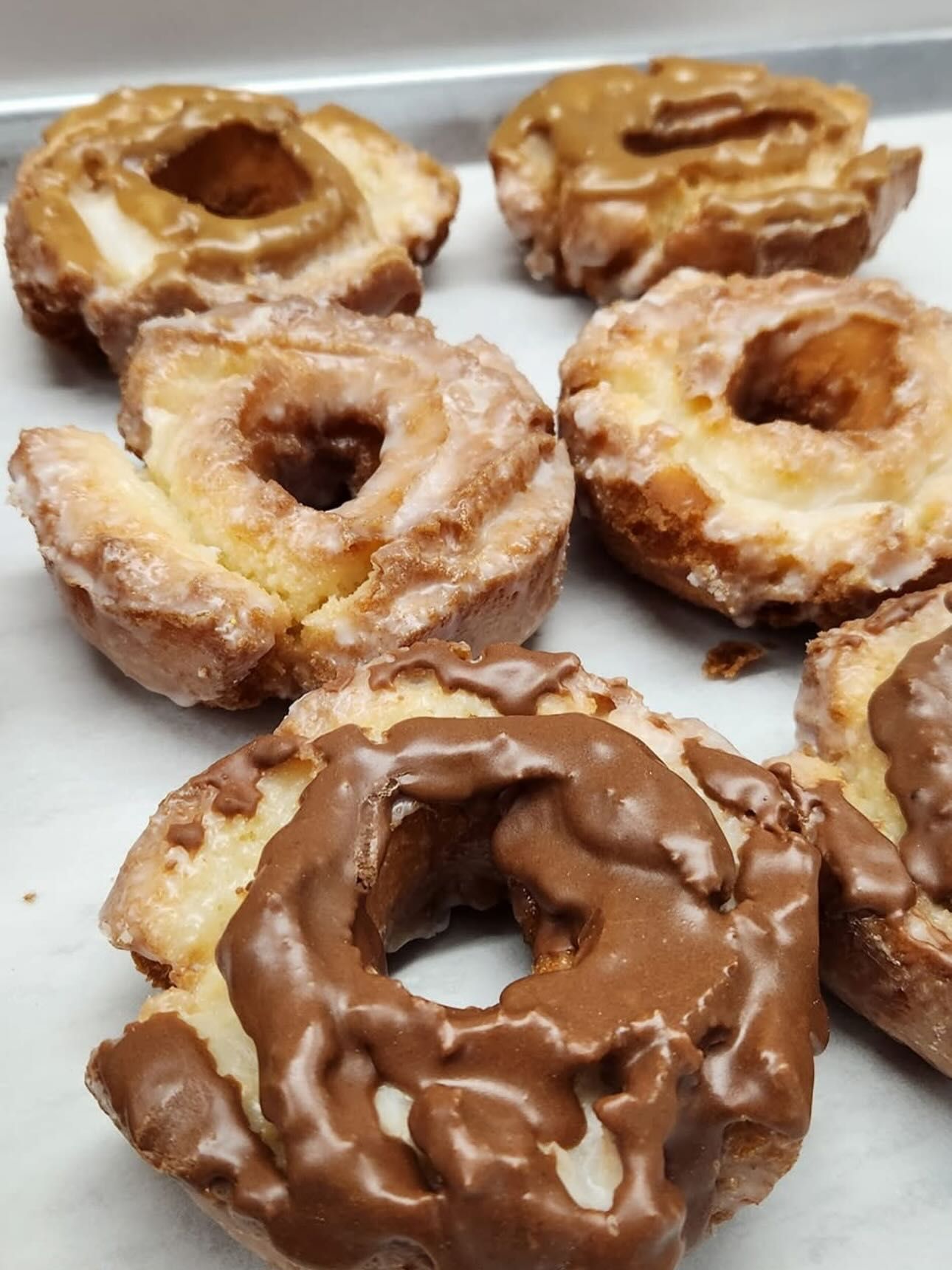 Glazed donuts with various toppings sit on a white surface.