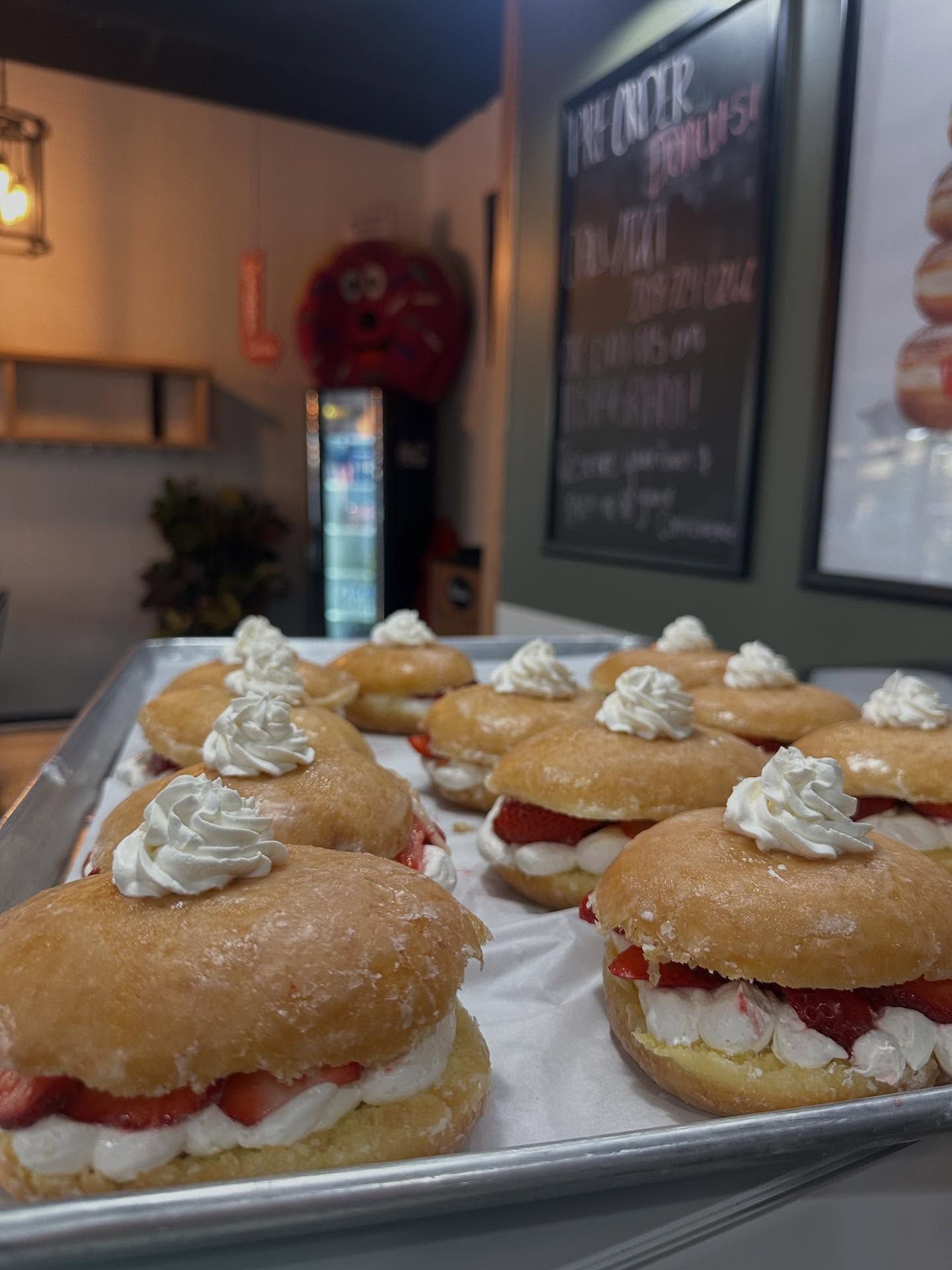 Tray of glazed doughnuts filled with cream and strawberries, topped with whipped cream. Bakery setting.