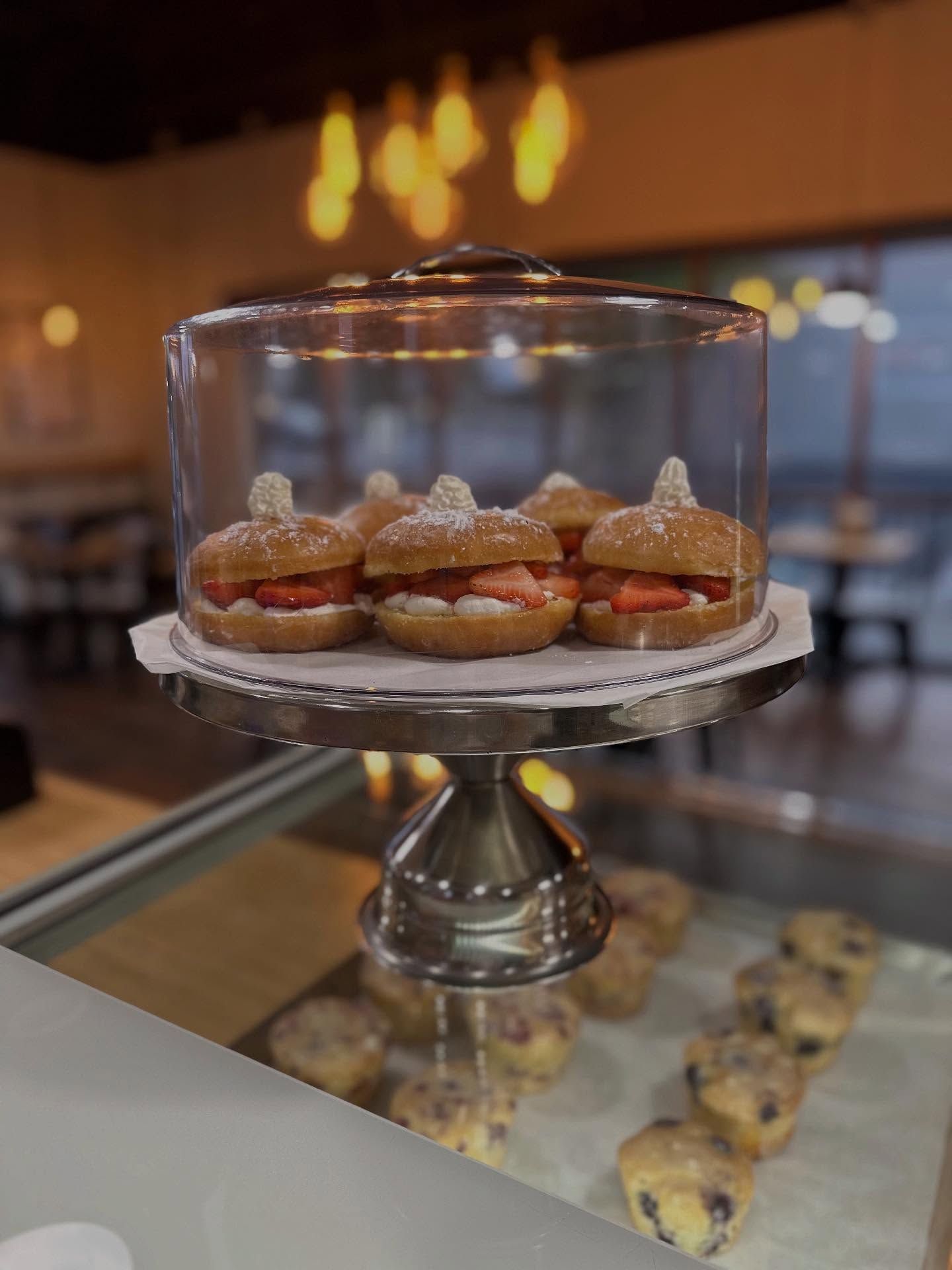 Strawberry cream-filled pastries on a tiered cake stand, inside a glass cloche, in a bakery display.