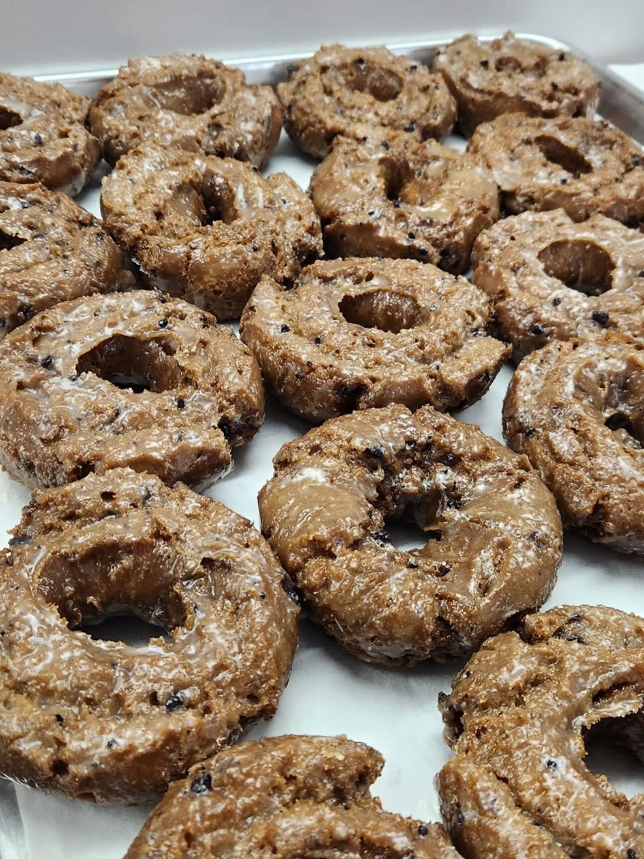 Tray of glazed, round chocolate doughnuts.
