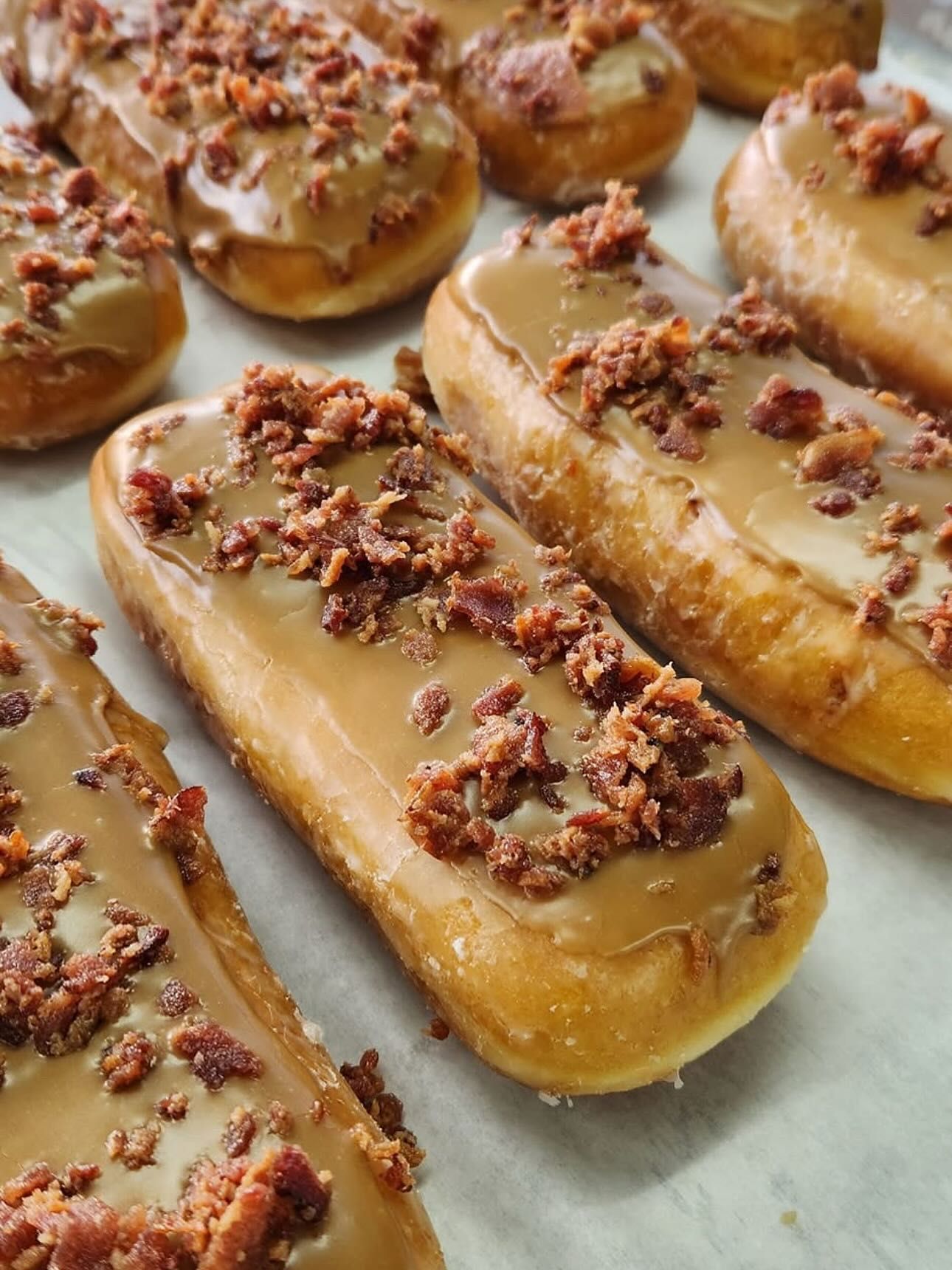 Glazed rectangular donuts topped with caramel frosting and crumbled bacon.